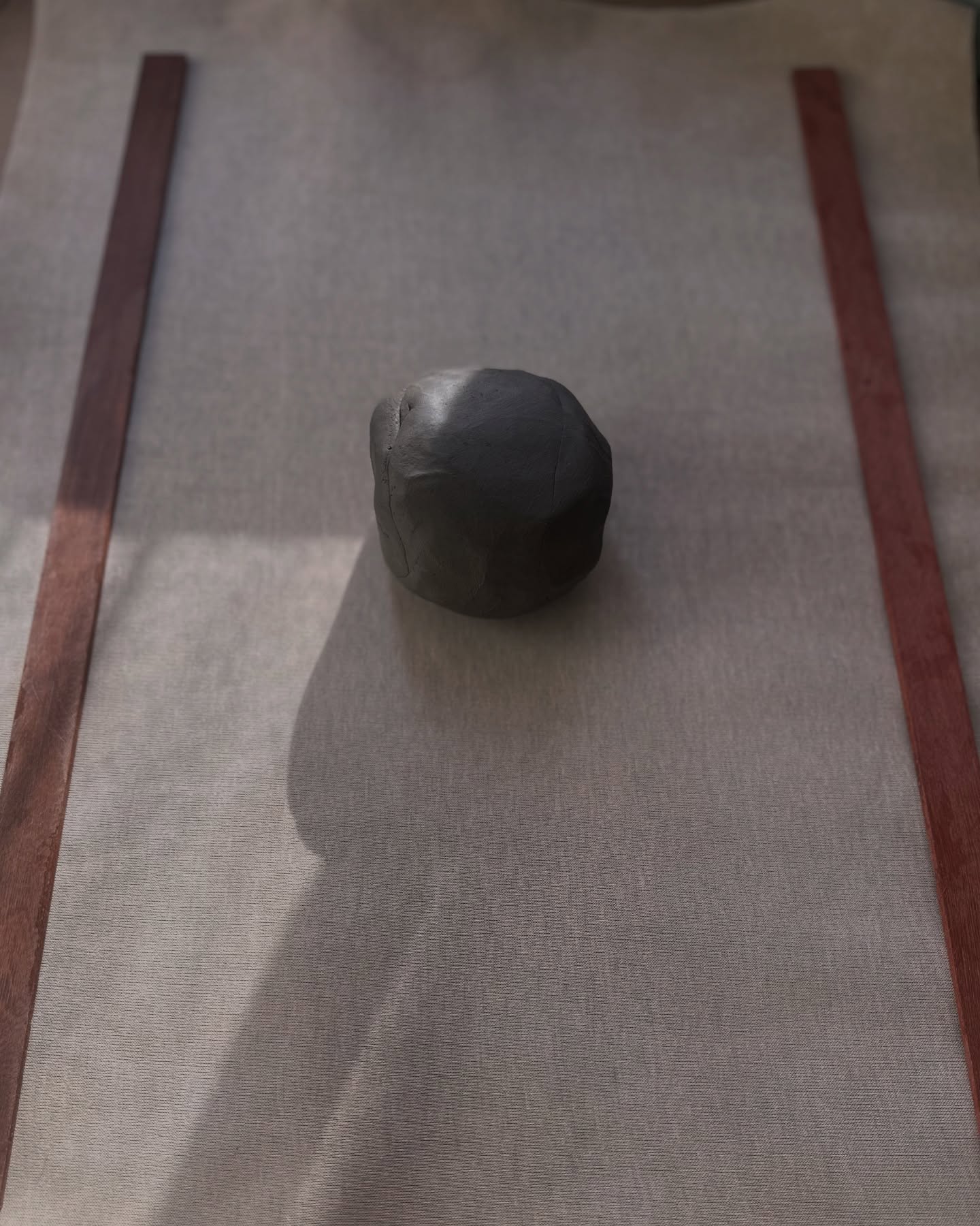 Bola de argila escura sobre a bancada, entre duas réguas de madeira