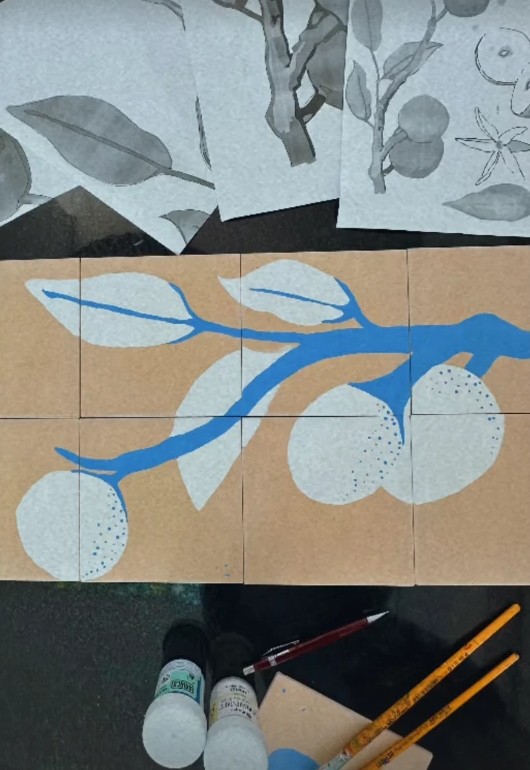 Azulejos cerâmicos pintados com um galho de mangaba em azul, ao lado dos estudos em aquarela