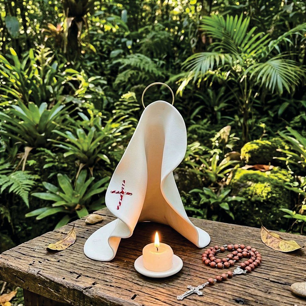 Manto de Maria branco com cruz bordada, vela e terço, em um jardim